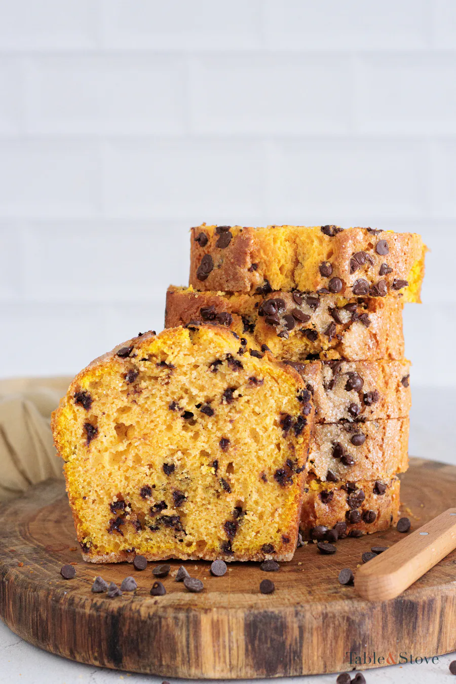 A slice of pumpkin bread with chocolate chips in the orange crumb, with more slices stacked behind it